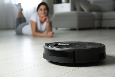 Modern robotic vacuum cleaner and blurred woman on background Stock Photos