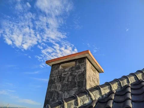 Modern Rooftop Chimney Under Clear Blue Sky with Soft White Clouds Stock Photos