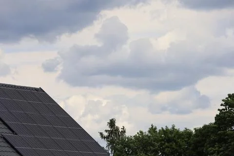 Modern rooftop solar panels installed on a house under a cloudy sky Stock Photos