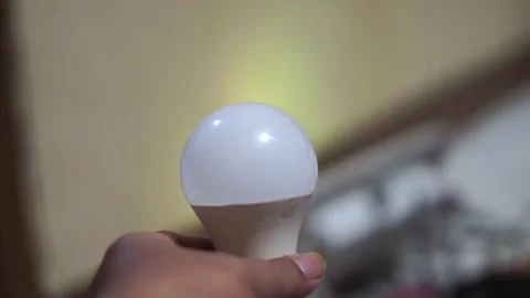 Modern round LED light bulb held in hand with soft lighting and a blurred Stock Footage 335591848