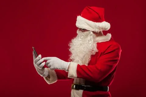Modern Santa Claus using tablet pc over red background. Christma Stock Photos