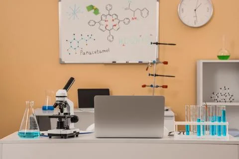 Modern science laboratory with microscope, laptop, and chemical formulas on w Фото