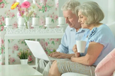Modern senior couple smiling while browsing on laptop. Stock Photos