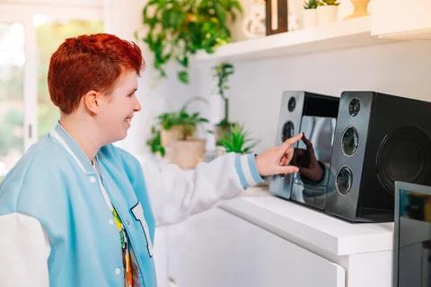 Modern, short-haired, red-haired, non-binary woman, turns on mini-system at home Stock Photos