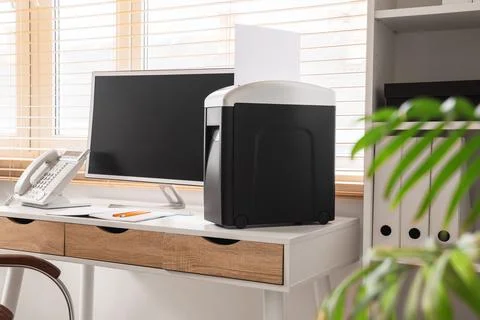 Modern shredder with paper and computer on desk in office 库存照片
