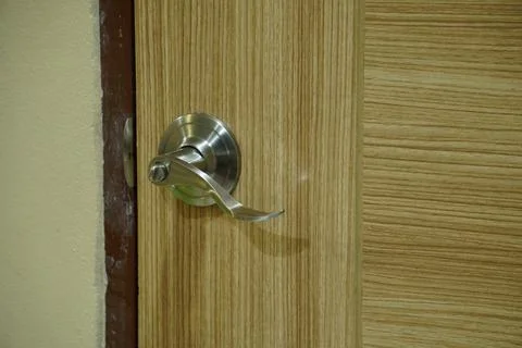 A modern silver door handle is installed on a light-colored wooden door. Photos