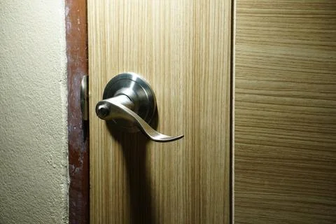 A modern silver door handle is installed on a light-colored wooden door. Photos