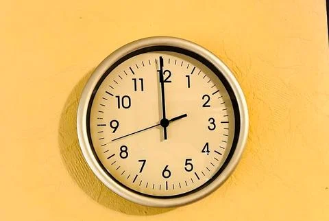 Modern Silver Frame Wall Clock on Yellow Textured Background Showing Twelve.. Stock Photos