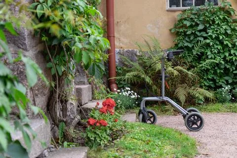 A modern silver rollator mobility aid stands parked on a gravel walkway in a  Stock Photos