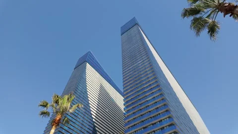 Modern skyscraper architecture with palm trees against blue sky Видео 334153530