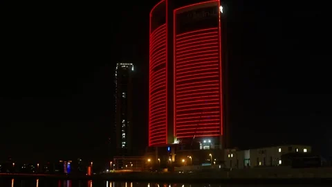 Modern skyscraper glows red neon light reflecting waterfront at night Stock Footage 337479727