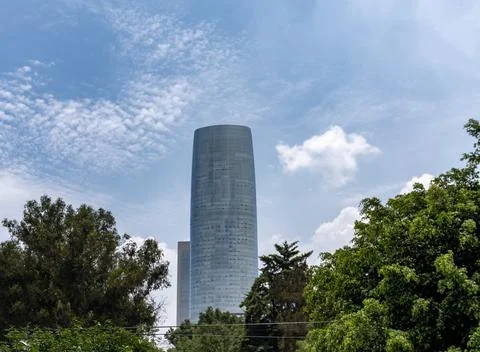 Modern Skyscraper: Low-Angle View of Torre Mítikah Framed by Green Trees Fotos de archivo
