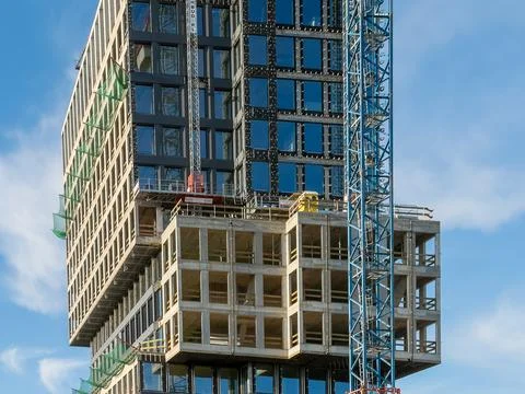 Modern skyscraper under construction with a tall blue crane against a sunny Stockfoto's