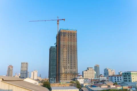Modern skyscraper under construction with a tall crane against a clear blue s Stock Photos