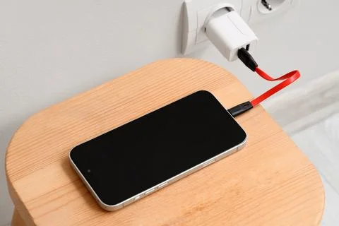 Modern smartphone charging with red cable and white adapter plugged into wall Stock Photos