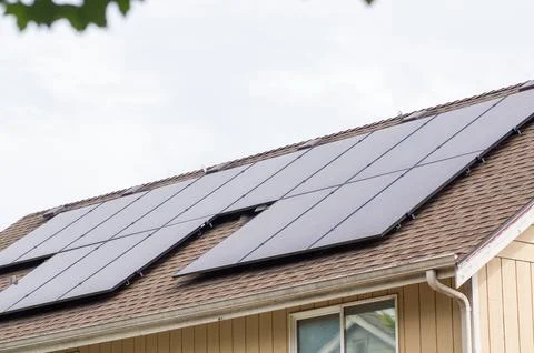 Modern solar panels installed on a brown shingled roof of a residential house Stock Photos
