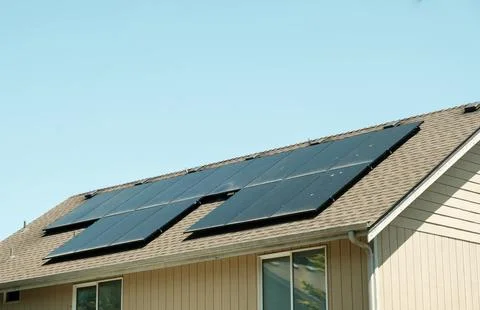 Modern solar panels installed on the shingled roof of a suburban house. Stock Photos