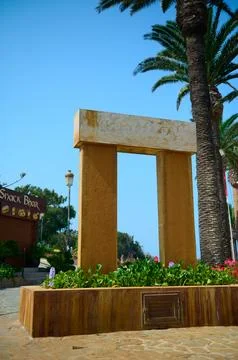 Modern stone arch monument framed by palm trees on a sunny Tangier promenade Photos