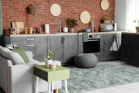 Modern studio apartment interior with a gray sofa, green side table, and a ki Stock Photos