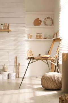 Modern studio interior with artist's workplace and wooden easel near large wi Foto stock
