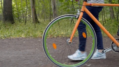Modern style bicycle being pushed in a park by a blonde woman Stock Footage