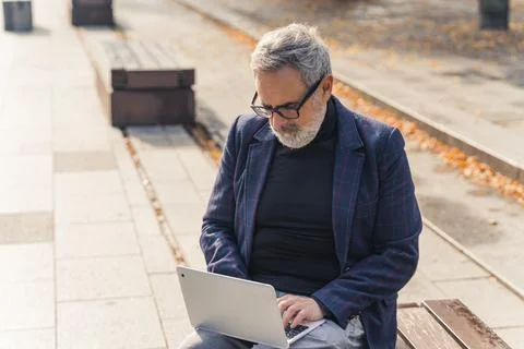 Modern stylish bearded grey-haired mature man entrepreneur sitting on a bench in Foto stock