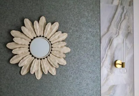 Modern sunburst wall mirror with feather petals on textured grey wall Stock Photos