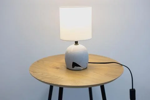 Modern table lamp with a cracked base stands on a wooden side table. Stock Photos