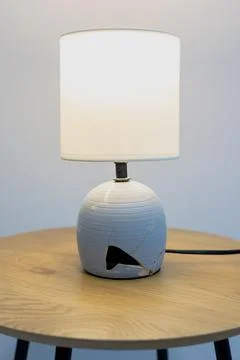 Modern table lamp with a cracked base stands on a wooden side table. Vertic.. Stock Photos