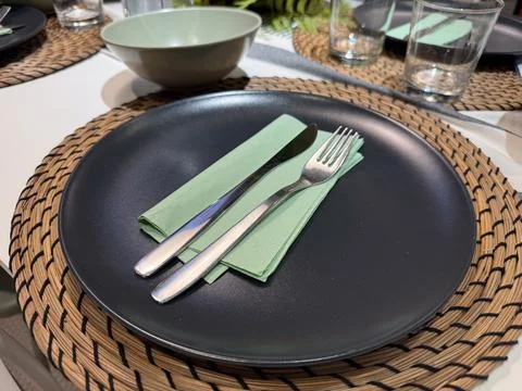 Modern table setting black plate green napkin fork knife on woven placemat Stock Photos
