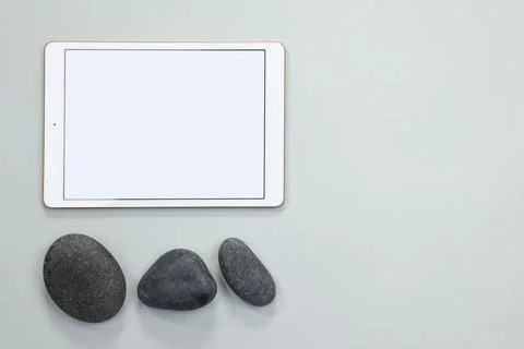 Modern tablet and pebbles on light grey background, flat lay. Space for text Stock Photos