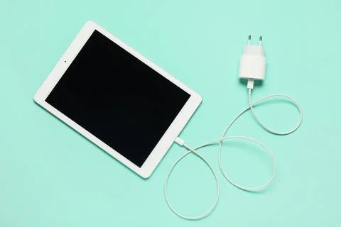 Modern tablet computer with blank screen and power adapter on turquoise backg Stock Photos