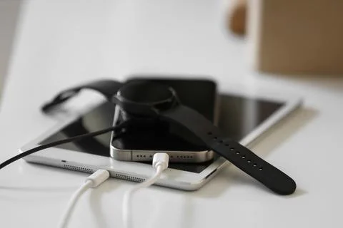 Modern tablet with mobile phone, charging cable and smartwatch on shelf in ro Stock Photos
