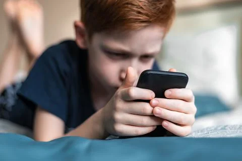 Modern technology hands of a red-haired boy child holding a mobile phone, wat Stock Photos