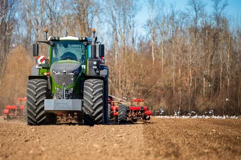 Modern tractor pulls red tillage rig in spring field preparation Stock Photos