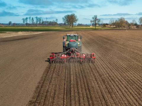 Modern tractor with seed drill forms parallel furrows on tilled field Stock Photos