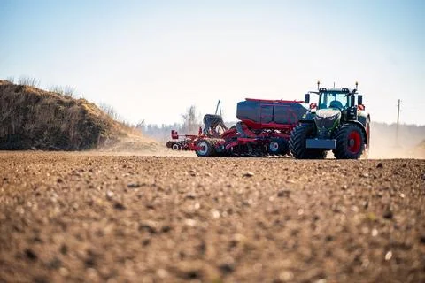 Modern tractor with seed drill seeding a wide tilled field in spring Stock Photos