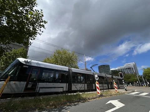Modern tram crossing urban intersection beside office towers and overhead wires Foto stock