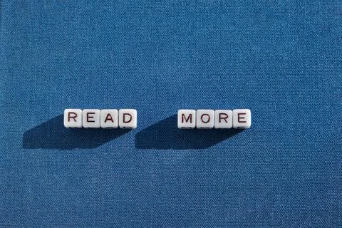 The modern trend READ MORE is lined with letter cubes on a beautiful fabric.. Stock Photos