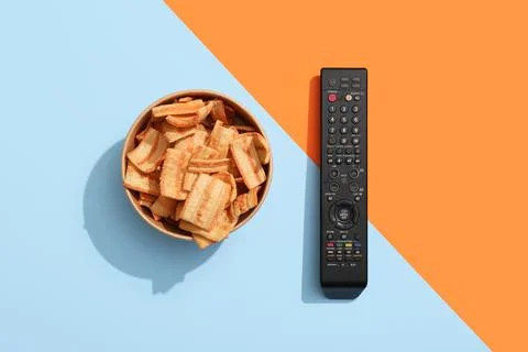 Modern TV remote control and bowl of potato chips on color background Stock Photos