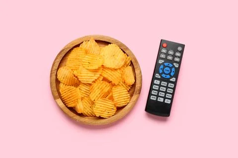 Modern TV remote control and board with potato chips on pink background Stock Photos