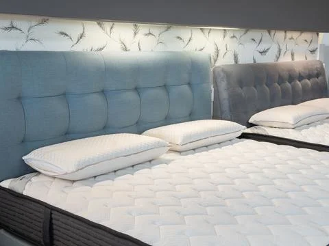 Modern upholstered bed frames with soft white pillows in a bright showroom, 库存照片