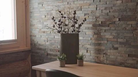 Modern vase with dry branches sitting on a wooden table against a stone wall in Stock-Footage 334713049
