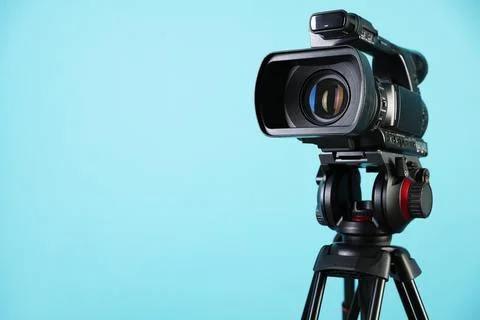 Modern video camera with tripod on light blue background, space for text Stock Photos