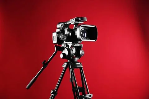 Modern video camera with tripod on red background, space for text Stock Photos