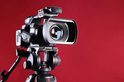 Modern video camera with tripod on red background, closeup. Space for text Stock Photos