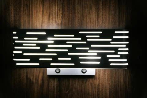 Modern wall-mounted light fixture with slotted black cover and bright white.. Stock Photos