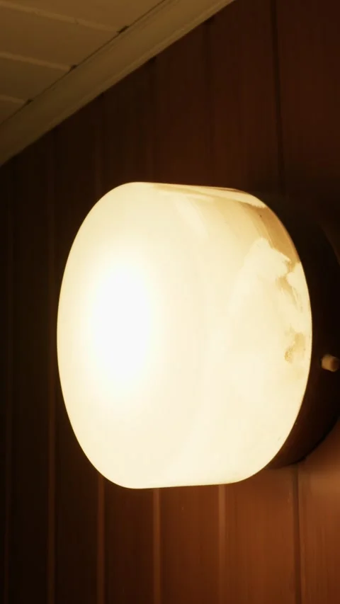 Modern Warm Circular Outdoor Light Fixture Glowing on Dark Wooden Wall Stock Footage 335641048