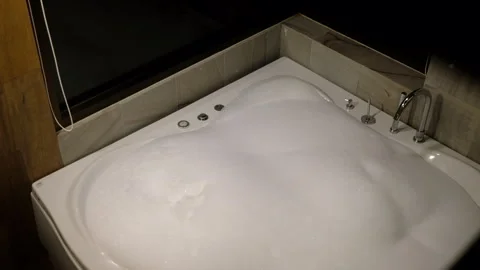 Modern whirlpool bathtub filling with white foam and bubbles with dimly lit Stock Footage 340276341