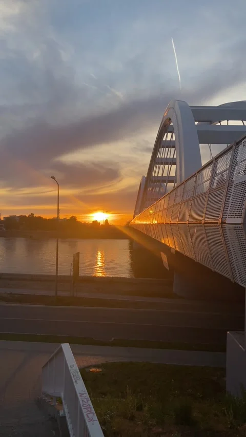 Modern white arch bridge spans river at sunset with golden light reflection Stock Footage 339480111
